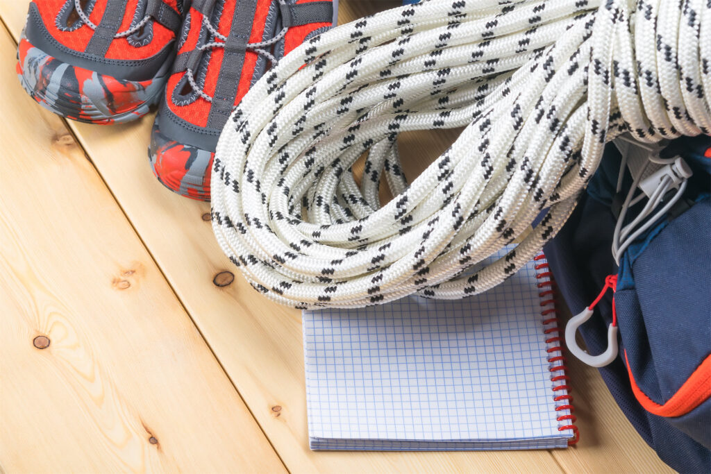 backpack, rope and shoes for hiking in the mountains and forests on a wooden light background